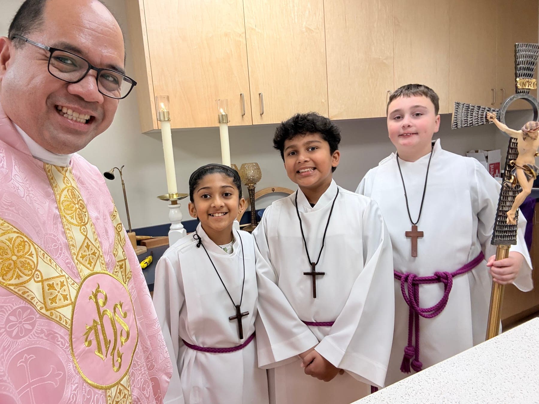 The priest smiling with a group of altar servers after Mass