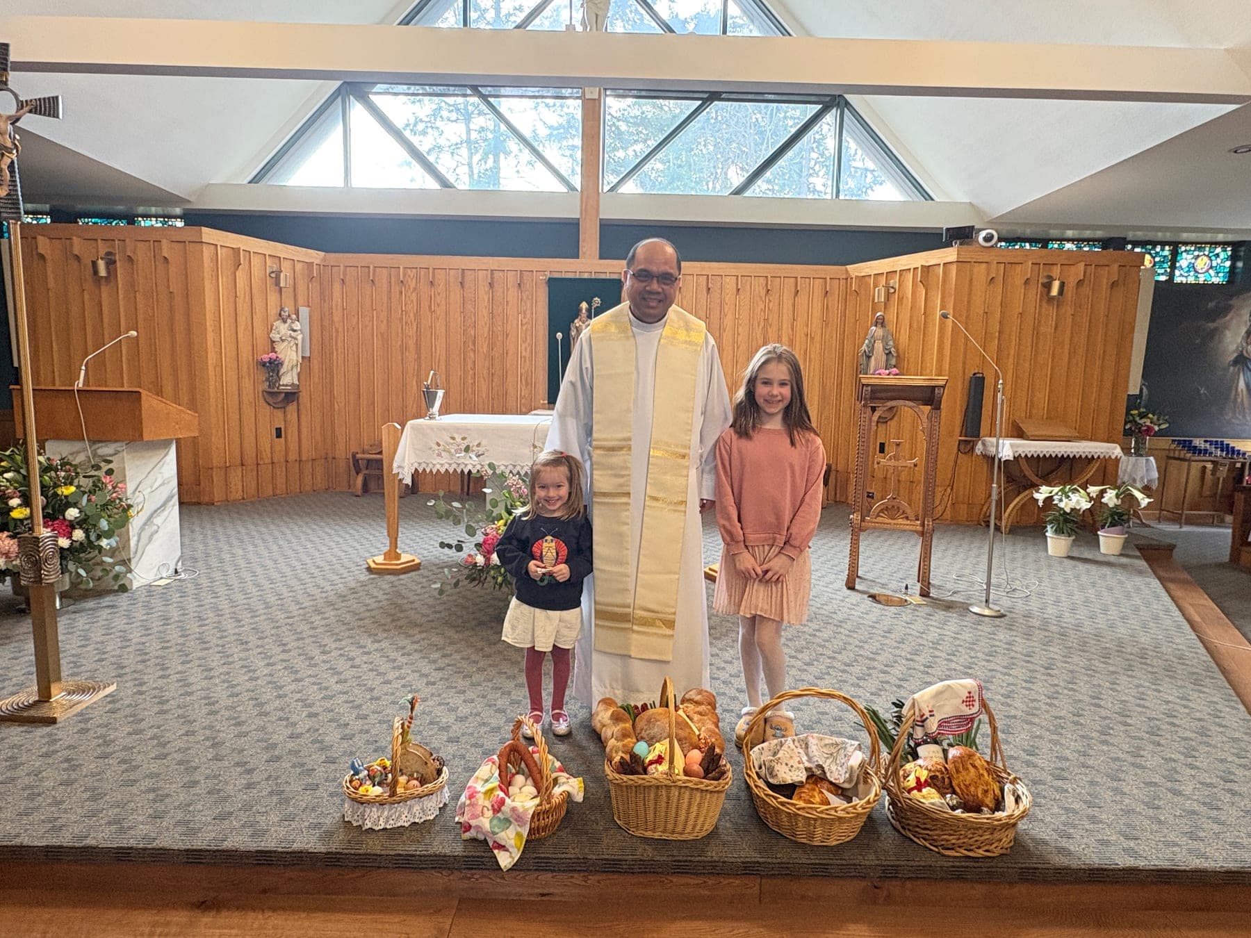 Children standing with the priest behind baskets of bread in the sanctuary