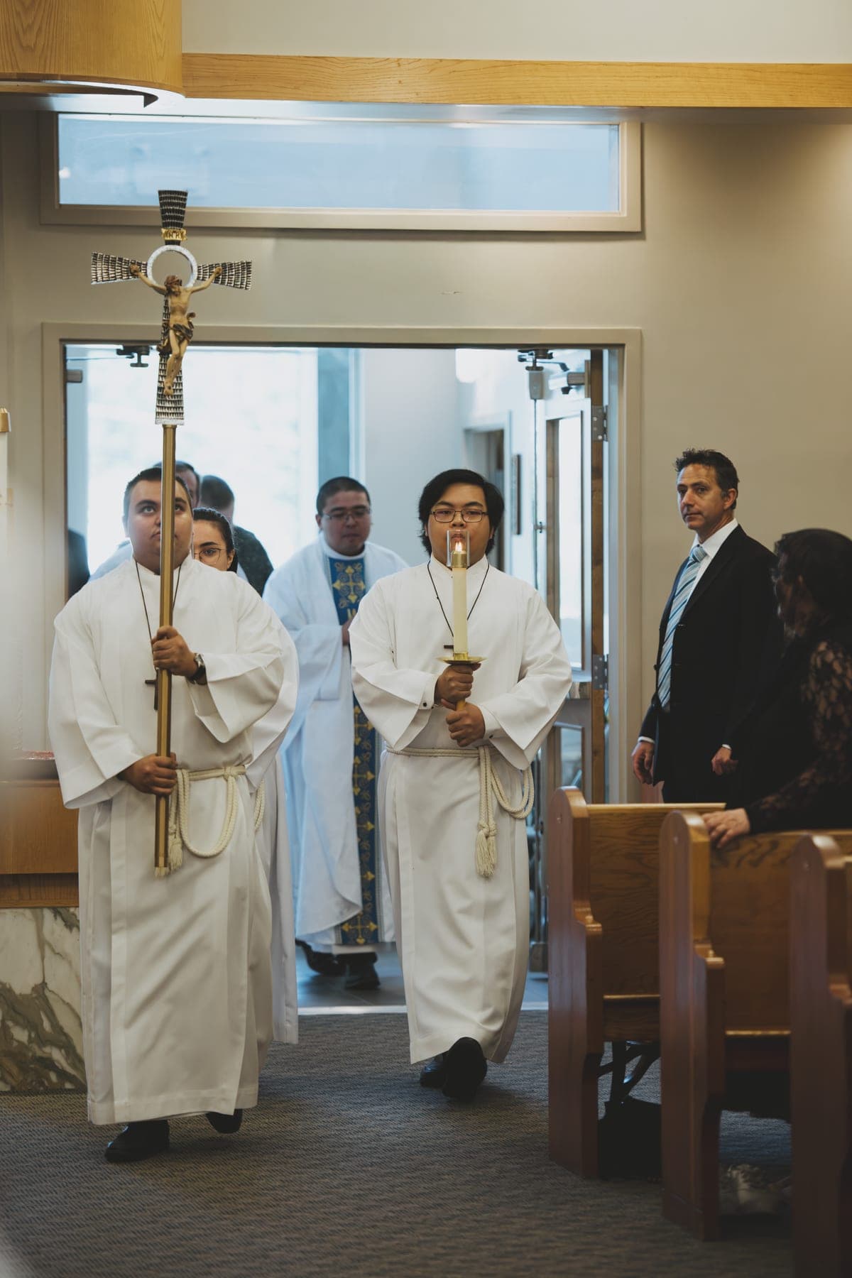 Altar servers carry the processional cross and candle through the doors as Mass begins