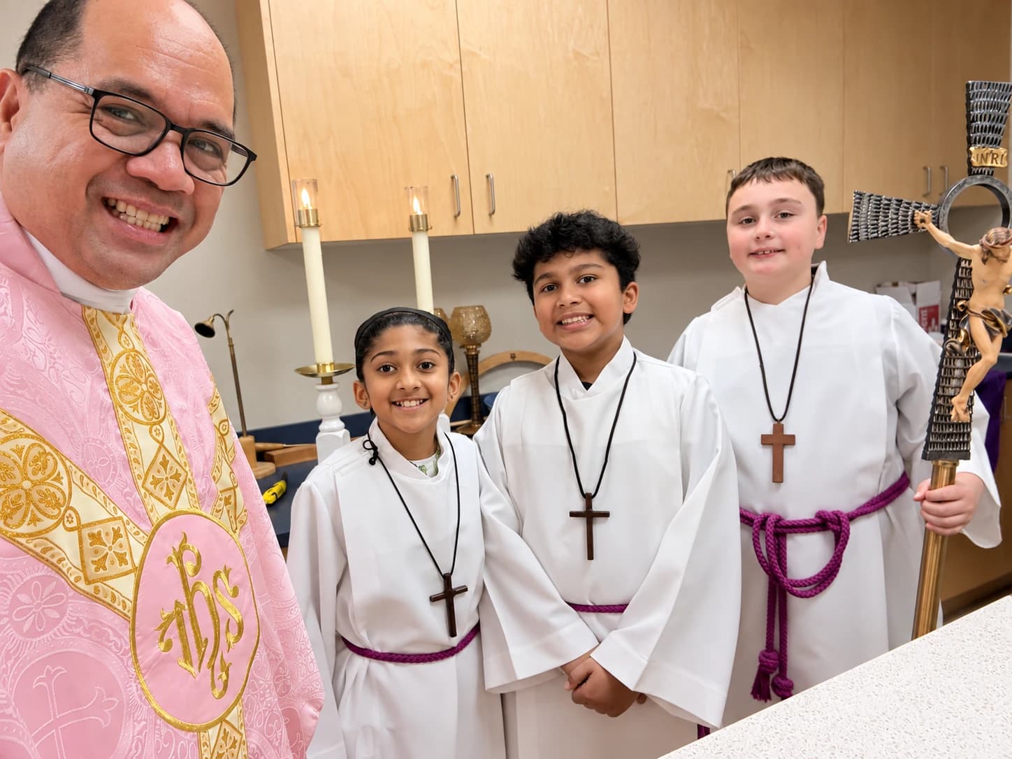 Father Mel smiling with three young altar servers in the sacristy