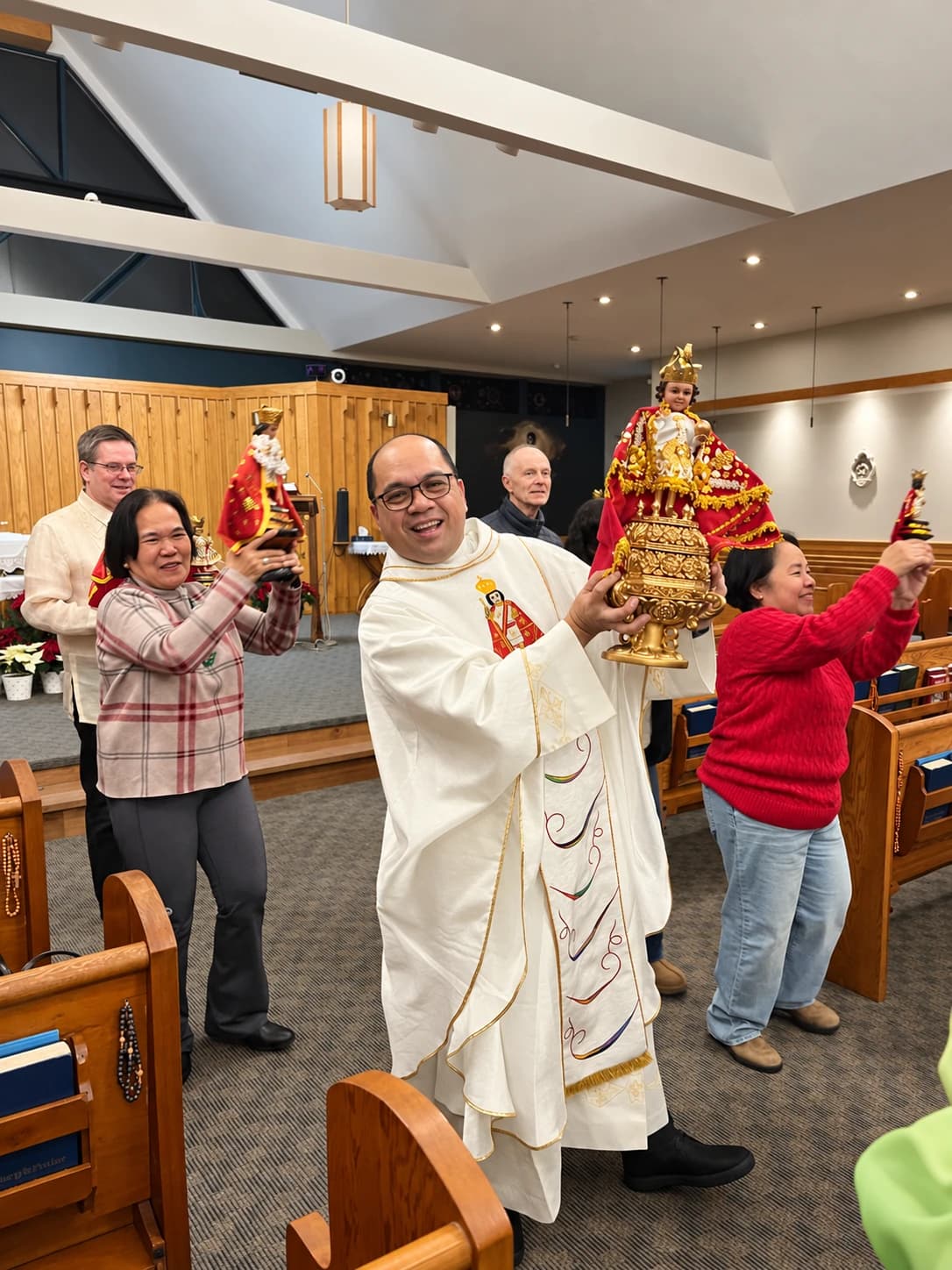 Father Mel joyfully carrying a statue of the Holy Child with parishioners inside the church