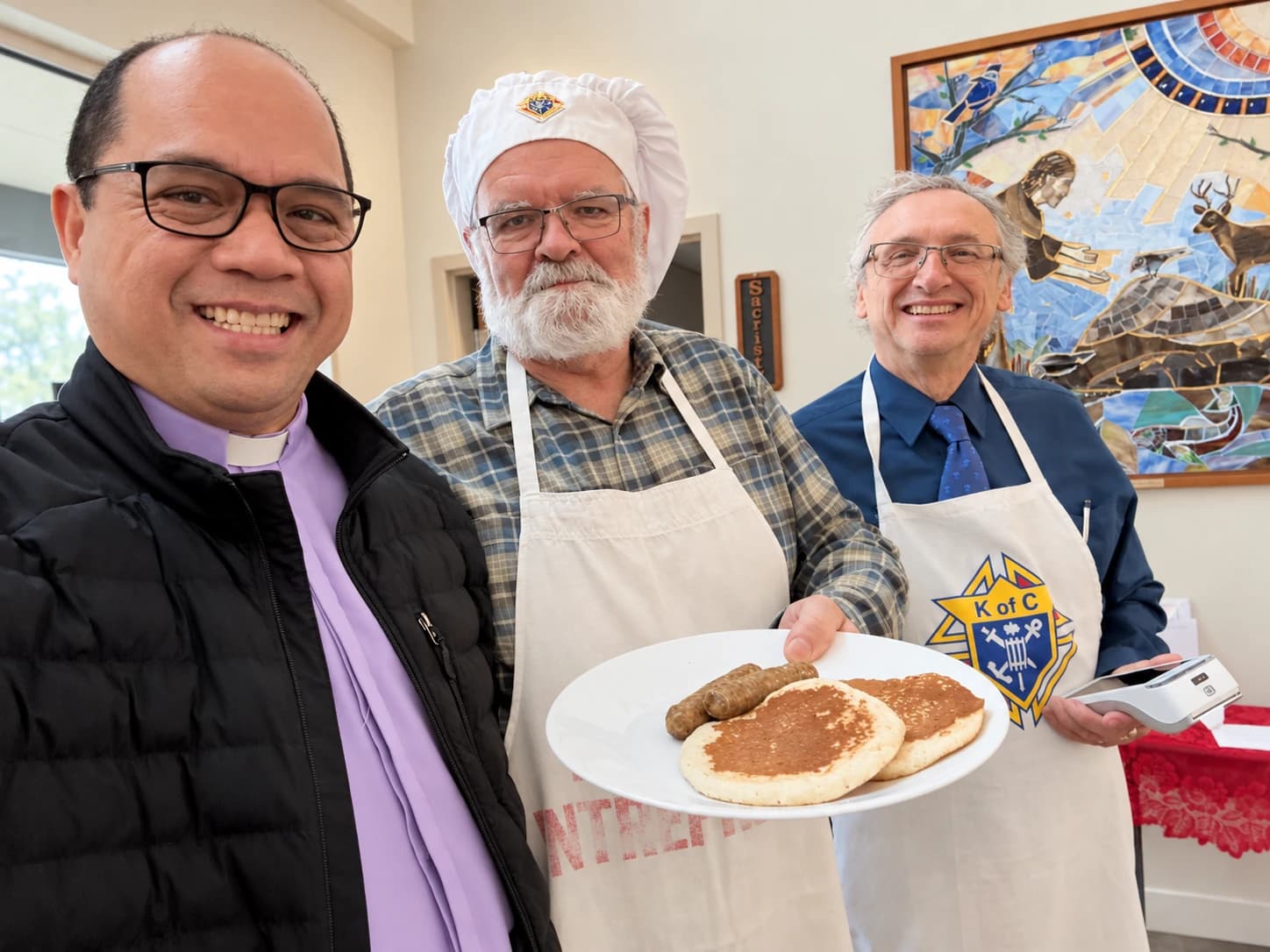 Father Mel smiling with parish volunteers at a community pancake breakfast