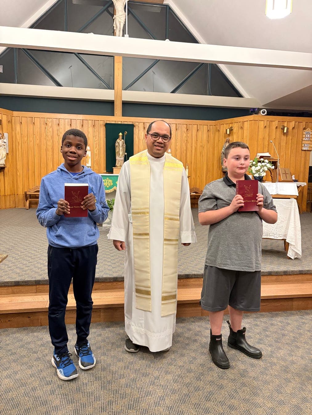 Two children holding their new Bibles beside the priest in the sanctuary