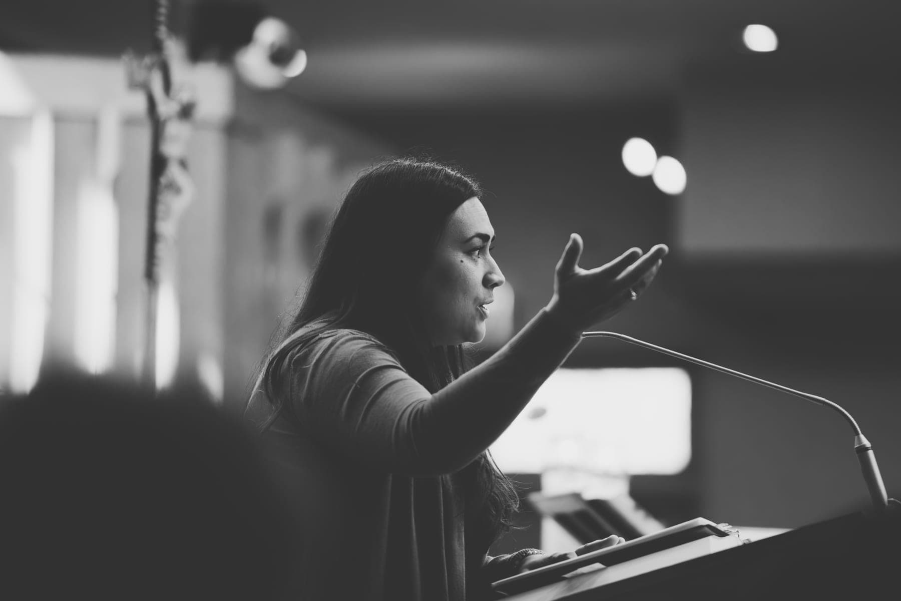 A parishioner proclaiming the reading at the ambo, hand raised, in black and white