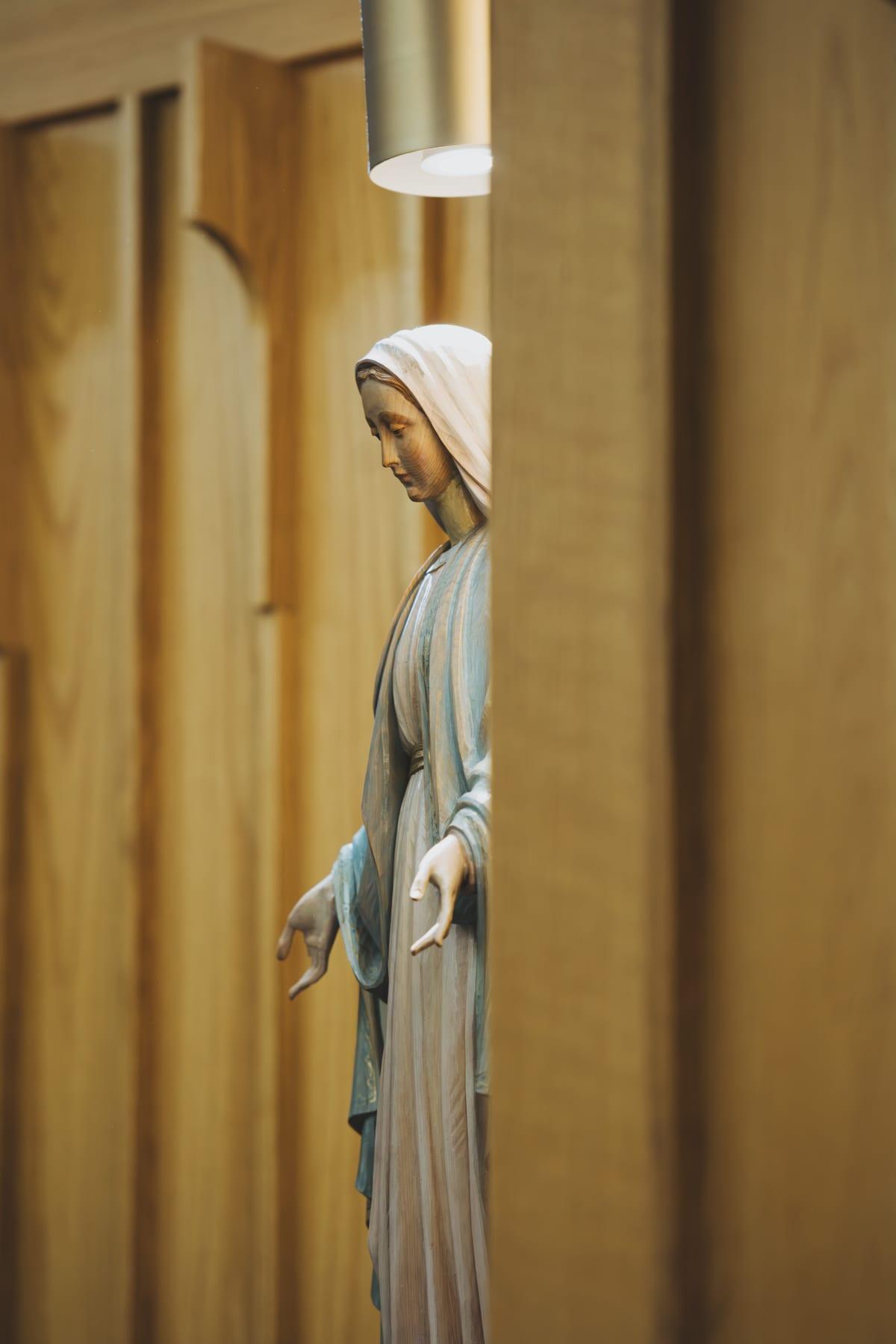 Statue of the Blessed Virgin Mary with open hands, framed between the cedar panels of the church wall