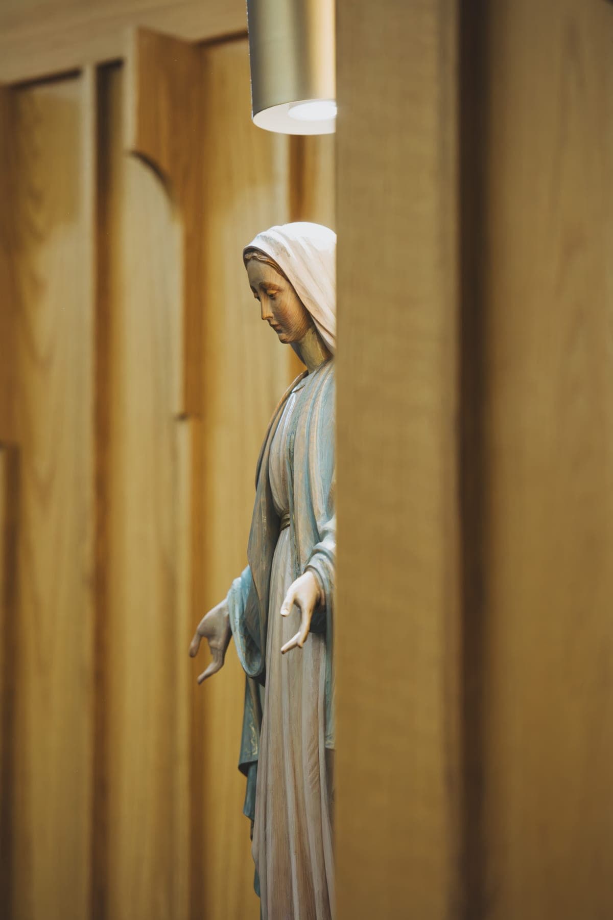 Statue of the Blessed Virgin Mary with open hands, framed between the cedar panels of the church wall