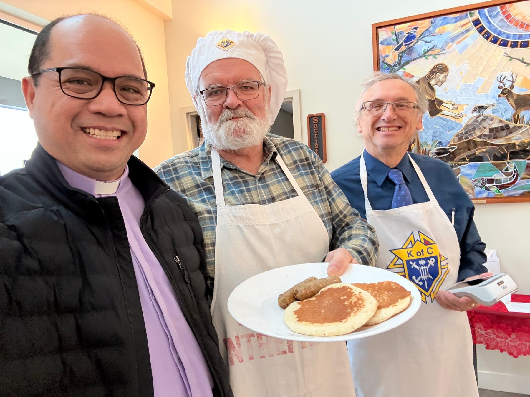 The priest and parish volunteers serving pancakes at a community breakfast