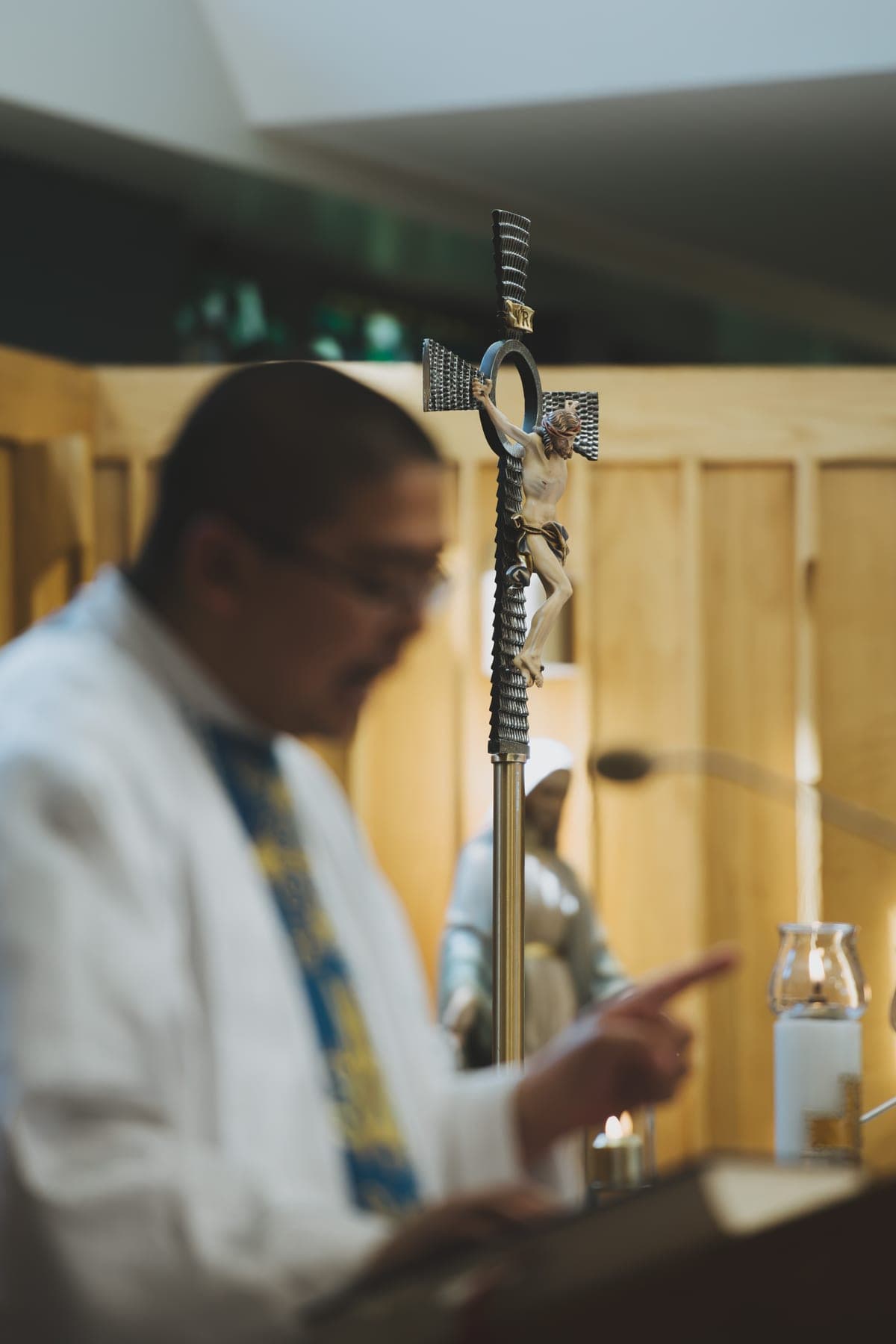 The priest reading at the ambo, with the processional cross in focus beside him