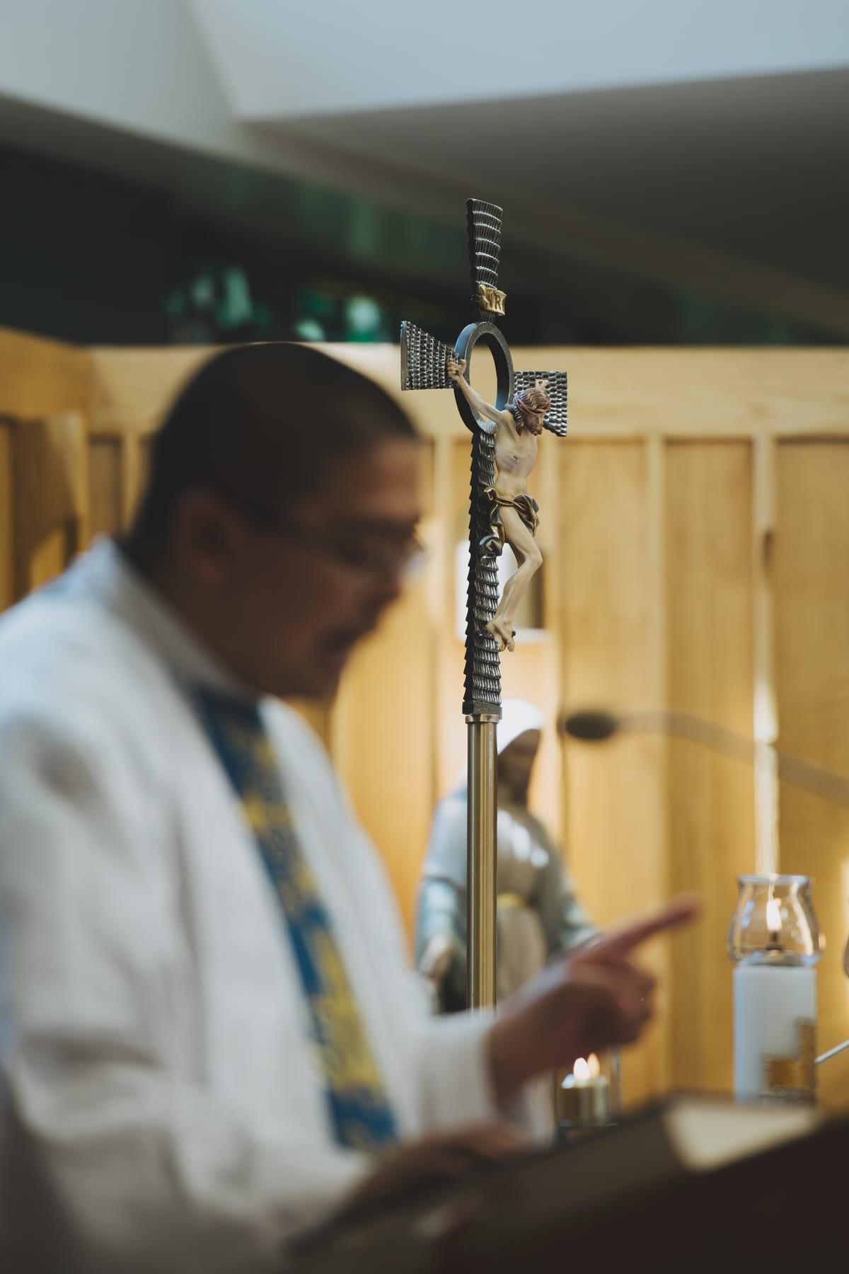 The priest reading at the ambo, with the processional cross in focus beside him