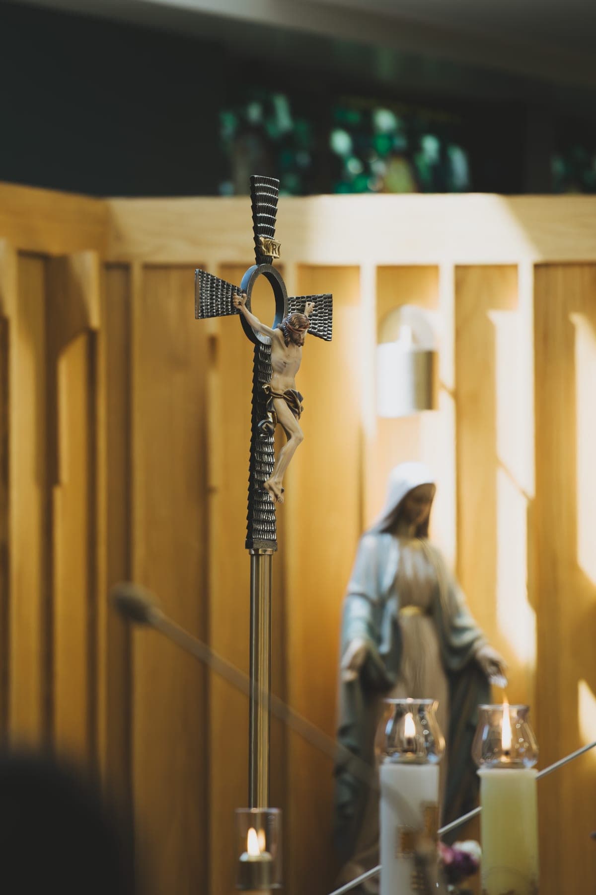 The processional cross standing in the sanctuary with the statue of Our Lady and lit candles behind it