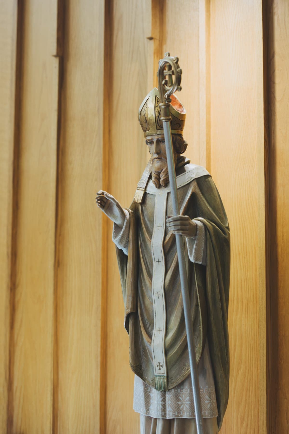 Carved statue of St. Patrick in green vestments holding a crosier, against the cedar wall of the church